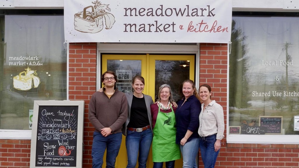Five people stand in front of Meadowlark Market and Kitchen in Lander, Wyoming, beside a chalkboard reading Open today