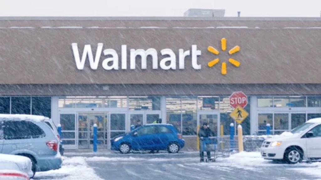 A Walmart storefront in falling snow, a shopper pushing a cart past parked cars